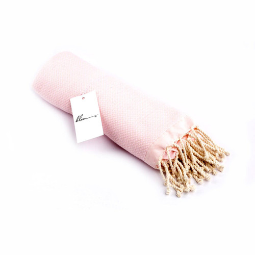 A rolled pink beach towel with tasselled edges and a branding tag attached.