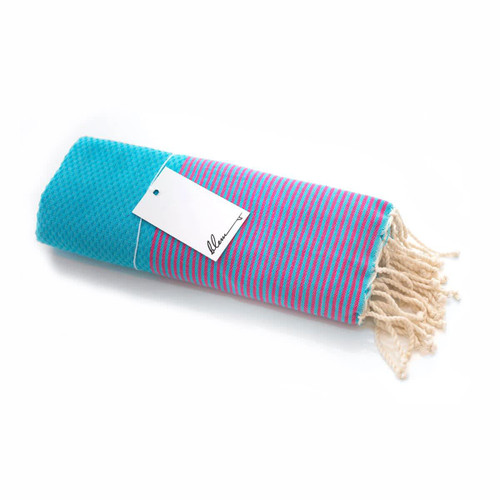 A rolled beach towel featuring vibrant stripes of pink and purple, with a solid turquoise end and fringed edges.