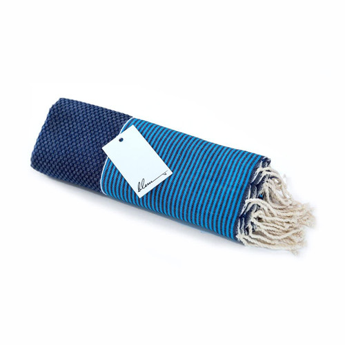 A rolled beach towel in blue and navy stripes, featuring fringe edges and a tag attached. A rolled beach towel in blue and navy stripes, featuring fringe edges and a tag attached.