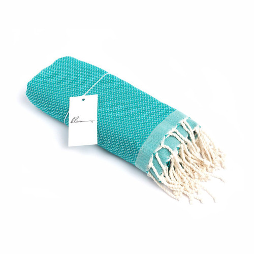A turquoise beach towel rolled and tied with fringe detail at one end, featuring a small tag. A turquoise beach towel rolled and tied with fringe detail at one end, featuring a small tag.