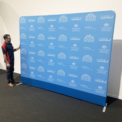 A straight tube fabric stand with a blue background and various logos, being adjusted by a person in a red and black shirt.