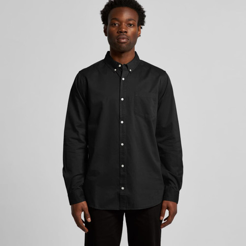 A black denim wash shirt featuring a button-up design and a chest pocket, modelled by a man.