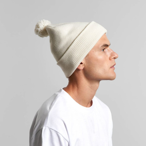 A white Pom Pom Beanie displayed on a model, featuring a fluffy pom pom on top and ribbed detailing. A white Pom Pom Beanie displayed on a model, featuring a fluffy pom pom on top and ribbed detailing.