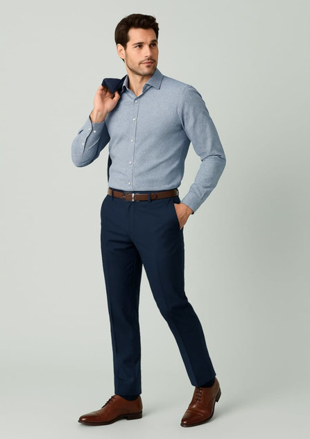A man in a light blue shirt and navy slim fit flat front pants, holding a dark blue item, wearing brown shoes.