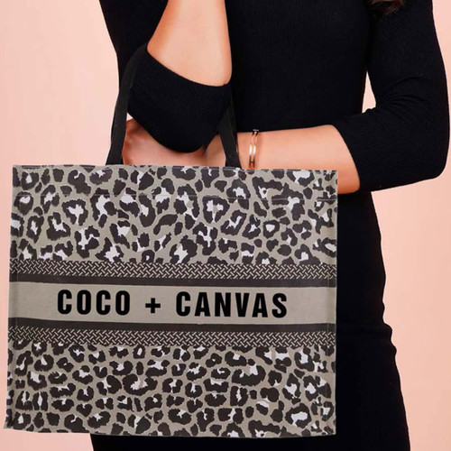 A stylish canvas tote bag in grey with a leopard print pattern and black handles, featuring a logo. A stylish canvas tote bag in grey with a leopard print pattern and black handles, featuring a logo.