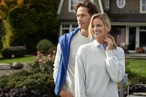 A grey crew neck sweatshirt is worn by a smiling woman outdoors, alongside a man in a blue sweatshirt.