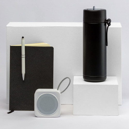 A black drink bottle, a black notebook, a white speaker, and a pen displayed on white pedestals.