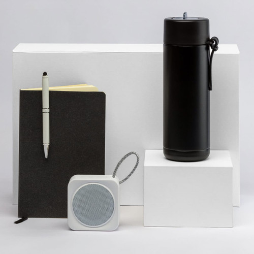 A black drink bottle, a black notebook, a white speaker, and a pen arranged on white pedestals. All products have branding.