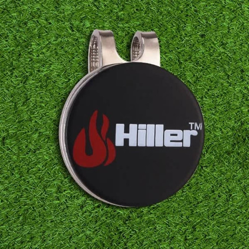 A black golf hat clip with a silver metal clip and a logo on the front, placed on green artificial grass.