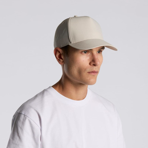 A beige nylon cap with a structured design worn by a person in a plain white T-shirt. It features a logo on the front.