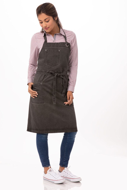 A dark grey bib apron with pockets, worn by a model, paired with a checked shirt and blue jeans.