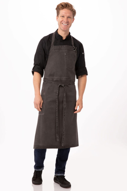A grey chef's bib apron with adjustable ties, worn by a model against a plain background. It features a front pocket and a logo.