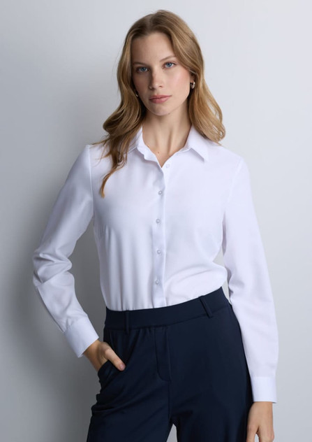 A women's long sleeve shirt in white with a button-up front and a collar, paired with dark pants.