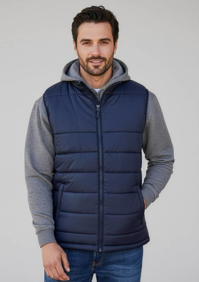 A man wearing a navy blue quilted alpine vest over a grey hoodie, with a casual expression.