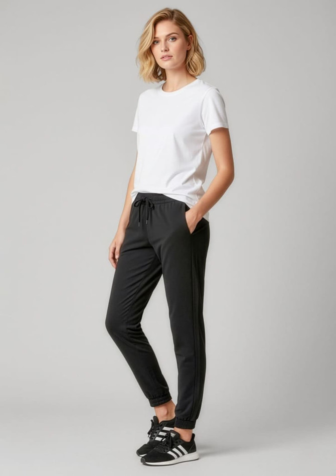 A model wearing women's black track pants paired with a white t-shirt, featuring a logo on the pants.