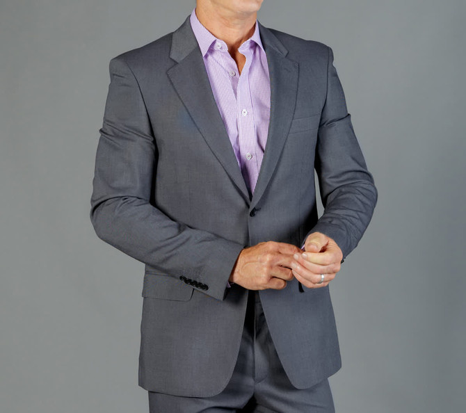 A grey suit jacket is worn over a light purple shirt, featuring a classic lapel design. The model adjusts the cuff.