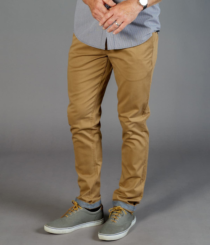 Tan chinos displayed on a model, featuring a slim fit and paired with grey shoes. The model wears a striped shirt.