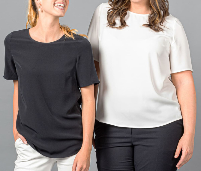 Two women wearing short sleeve shirts in black and white, standing side by side against a grey background.
