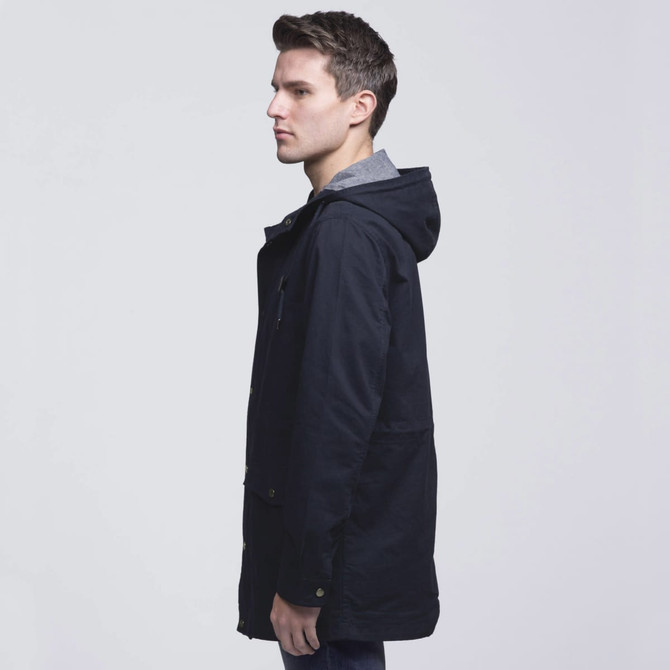 A twill jacket in navy blue featuring a hood, side pockets, and a grey inner lining. It has a logo on the front. A twill jacket in navy blue featuring a hood, side pockets, and a grey inner lining. It has a logo on the front.