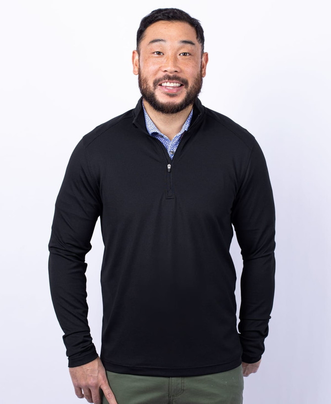 A man is wearing a black half-zip jacket with long sleeves and a logo on the chest. A man is wearing a black half-zip jacket with long sleeves and a logo on the chest.