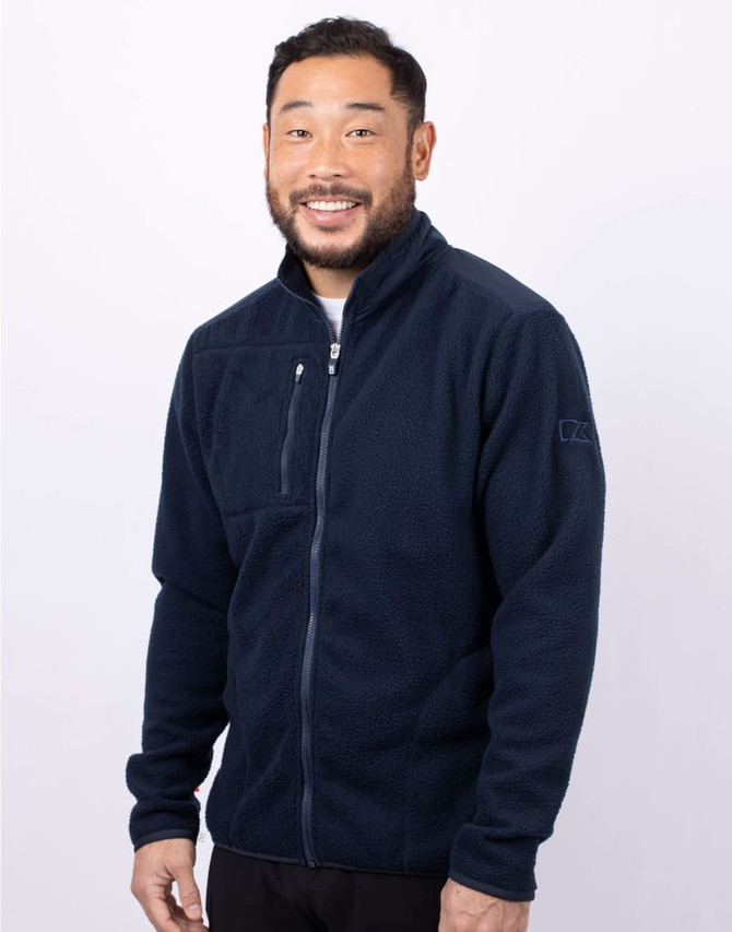 A man wearing a navy blue eco Sherpa jacket with a zippered front and a logo on the sleeve.