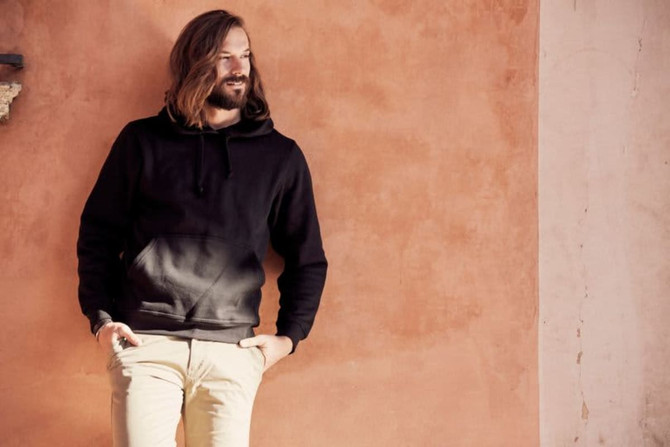 A black Stockholm hoodie displayed on a model against a warm-toned wall, featuring a front pocket and drawstring hood. A black Stockholm hoodie displayed on a model against a warm-toned wall, featuring a front pocket and drawstring hood.