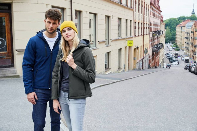Men's Equinox Softshell Jacket in navy, paired with a woman in a dark green version, both standing on a city street.