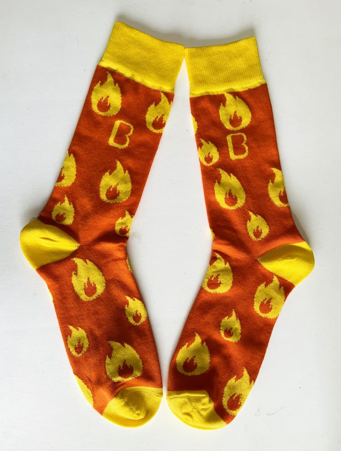 A pair of orange socks with yellow flame patterns and a yellow cuff, featuring a logo.