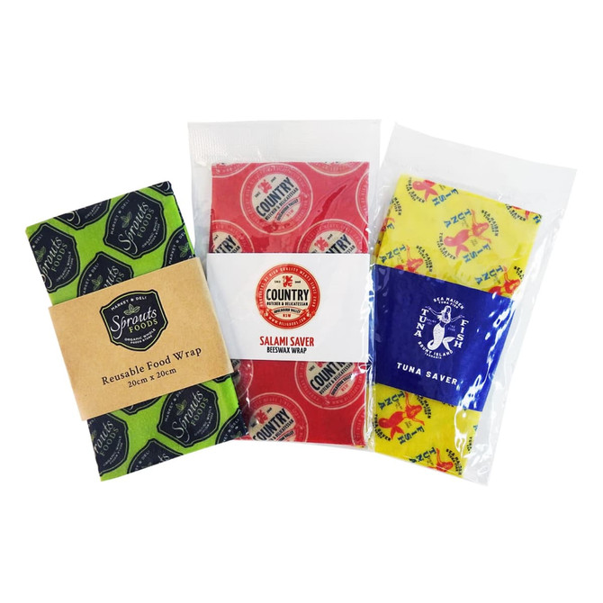 Three beeswax wraps in green, red, and yellow patterns, packaged for reusable food storage. Each features a distinct design and branding.