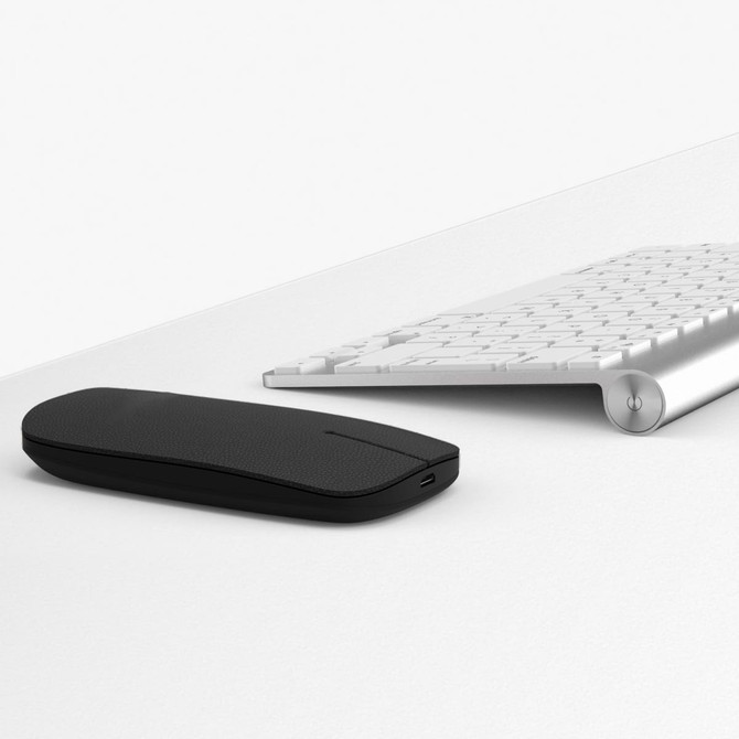 A black wireless mouse placed next to a silver keyboard on a white surface, featuring a sleek, minimalist design.