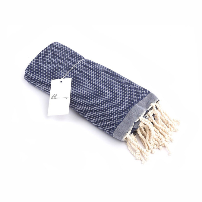 A rolled Indigo beach towel with a textured pattern and fringed edges, featuring a tag.
