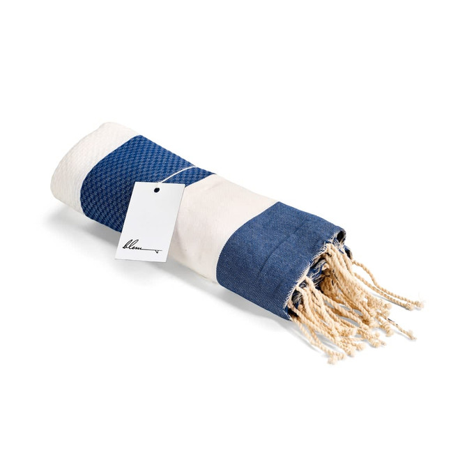 A rolled navy and cream beach towel with a woven texture and tasselled edges, featuring a tag.