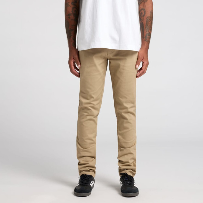 Beige standard pants worn by a person with tattoos, paired with black sneakers and a white t-shirt. Beige standard pants worn by a person with tattoos, paired with black sneakers and a white t-shirt.