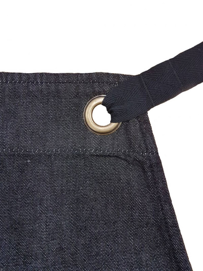 A dark denim bib apron featuring a metal grommet for adjustable ties. It includes a branding logo. A dark denim bib apron featuring a metal grommet for adjustable ties. It includes a branding logo.