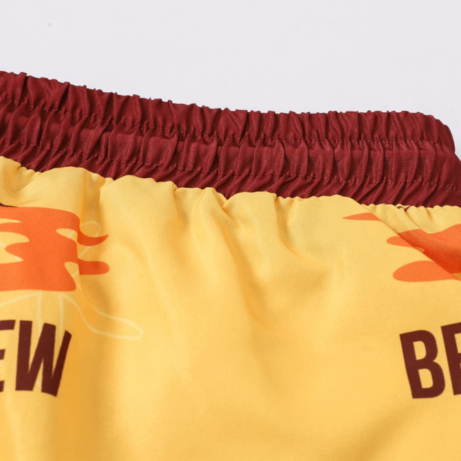 Men's polyester board shorts in yellow with maroon elastic waistband, featuring a logo and colourful graphics.