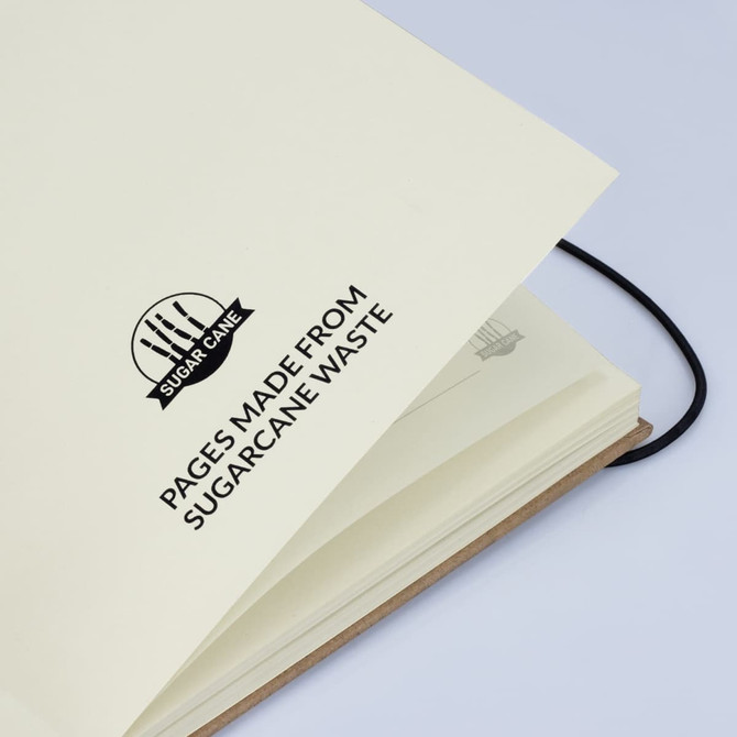 A cream-coloured hardcover notebook with a black elastic band, featuring sugarcane waste pages and a logo. A cream-coloured hardcover notebook with a black elastic band, featuring sugarcane waste pages and a logo.
