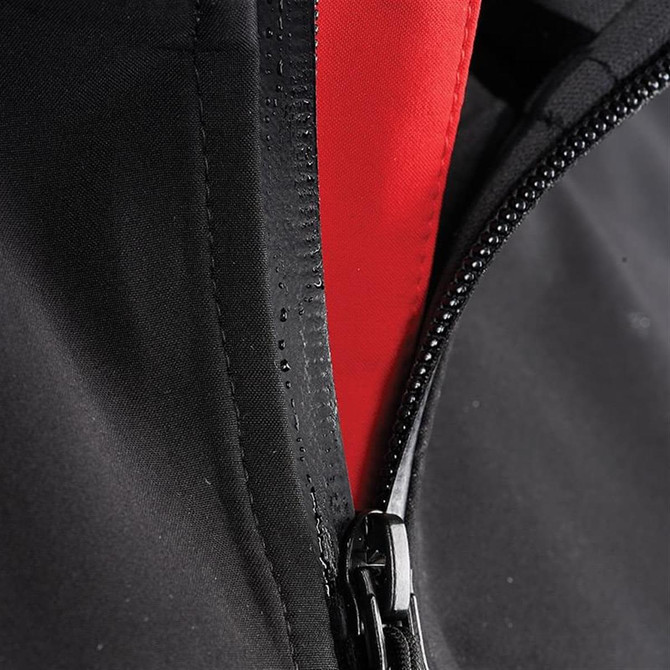 A close-up of a black softshell jacket featuring a red interior and a zippered front. The jacket has a logo.