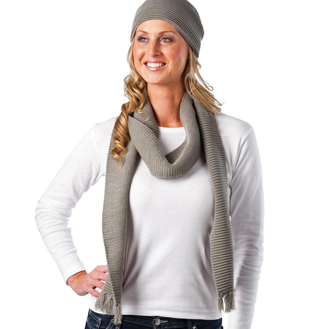 A woman wearing a grey knitted scarf and beanie, with her hair cascading down and a white long-sleeve top.