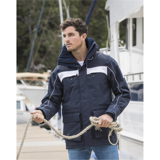 A unisex navy rain jacket with white accents, featuring a hood and multiple pockets, displayed outdoors near boats.