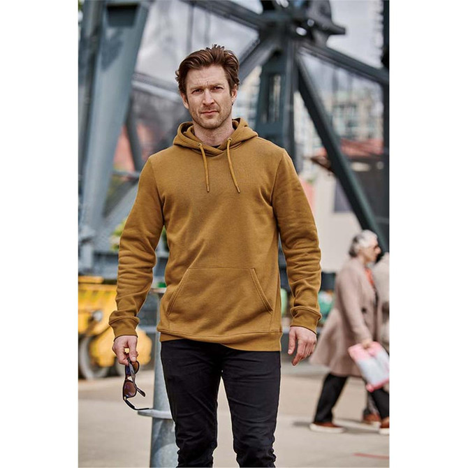 A man wearing a brown fleece pullover hoody with a front pocket, standing outdoors near industrial scenery.
