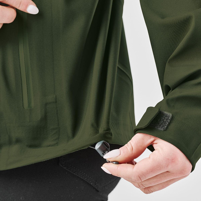 A green Women's Vertex Stormshell jacket with a person adjusting the bottom hem, featuring a logo.