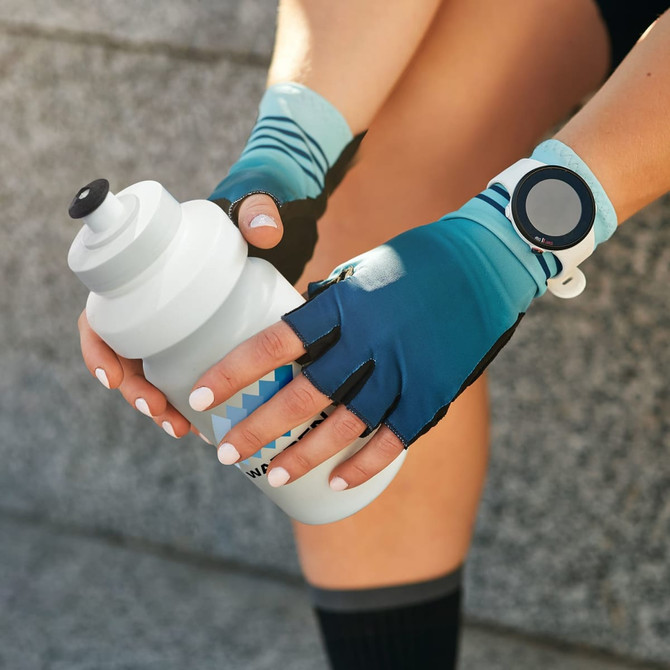 A drink bottle in a gradient of white and light blue, held by a person wearing blue fingerless gloves.