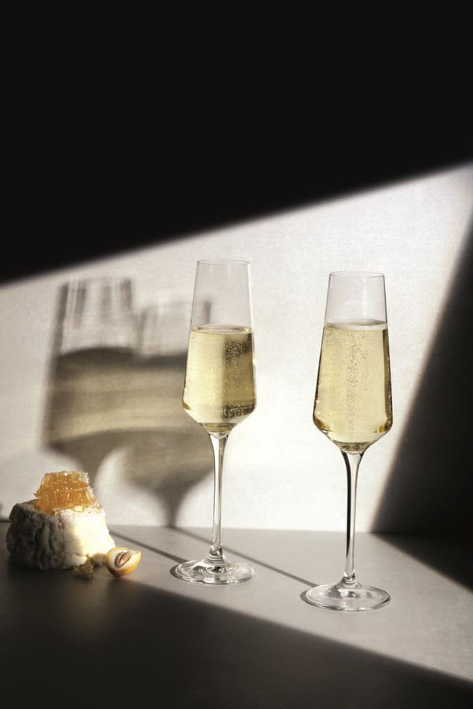 Two elegant crystal champagne flutes with a light golden beverage, alongside a piece of cheese and a honeycomb.