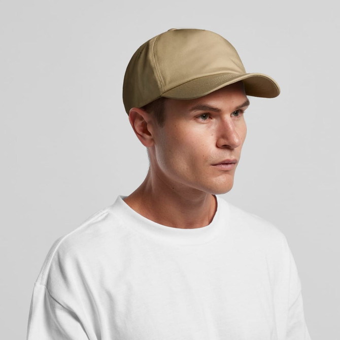 A beige cap is worn by a man with short hair, featuring a curved brim and a logo on the front. A beige cap is worn by a man with short hair, featuring a curved brim and a logo on the front.
