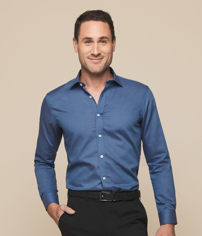 A button-up shirt in a rich blue shade, featuring a classic collar and long sleeves. The model displays a cheerful smile.