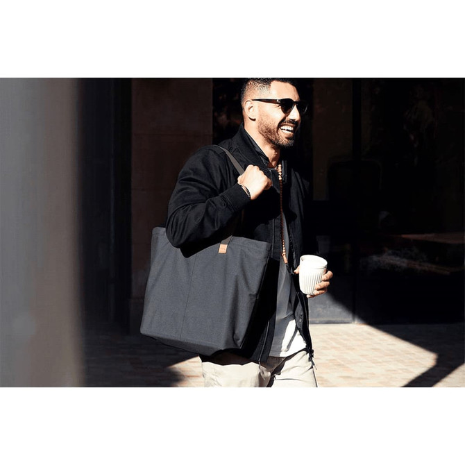 A stylish black tote bag held by a man with sunglasses, carrying a coffee cup while walking outside.