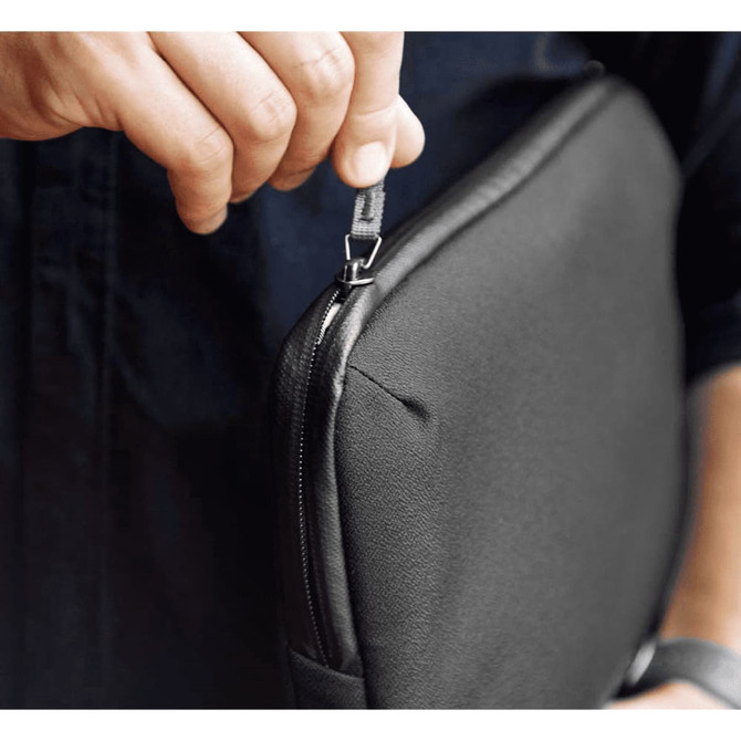 A person holding a black laptop caddy, highlighting the zip closure detail. The caddy has a sleek design and branding.