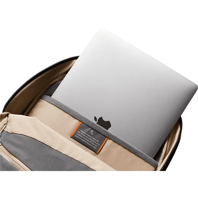 A silver laptop is nestled in the padded compartment of a tan and grey backpack, which features a logo.