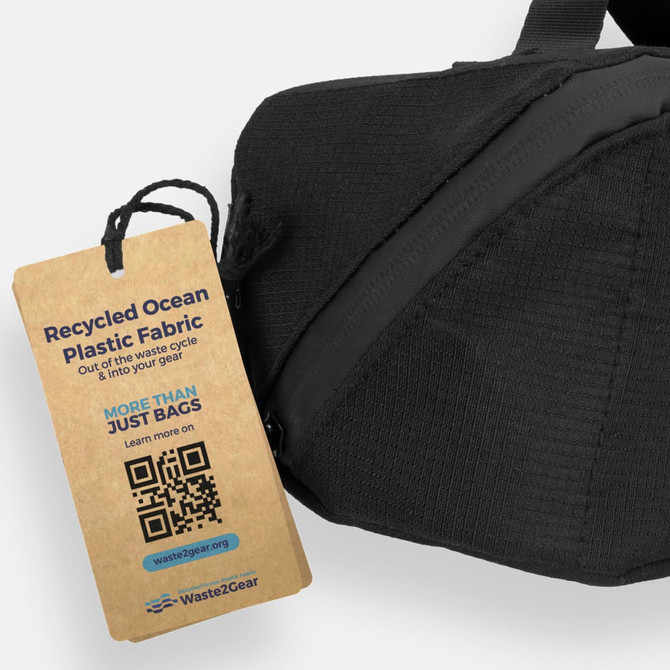 A black toiletry bag with a tag highlighting its recycled ocean plastic fabric. The bag features a logo.
