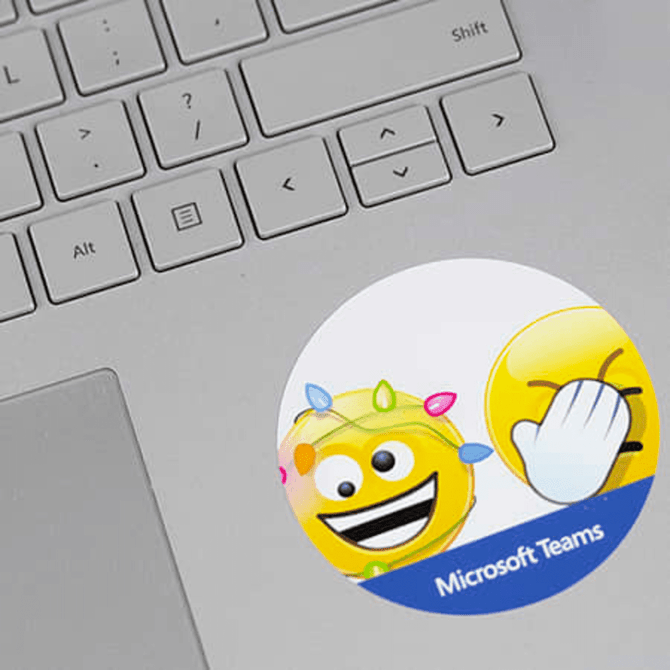 A round sticker featuring emojis and a logo, placed on a silver laptop keyboard. The sticker has bright colours. A round sticker featuring emojis and a logo, placed on a silver laptop keyboard. The sticker has bright colours.